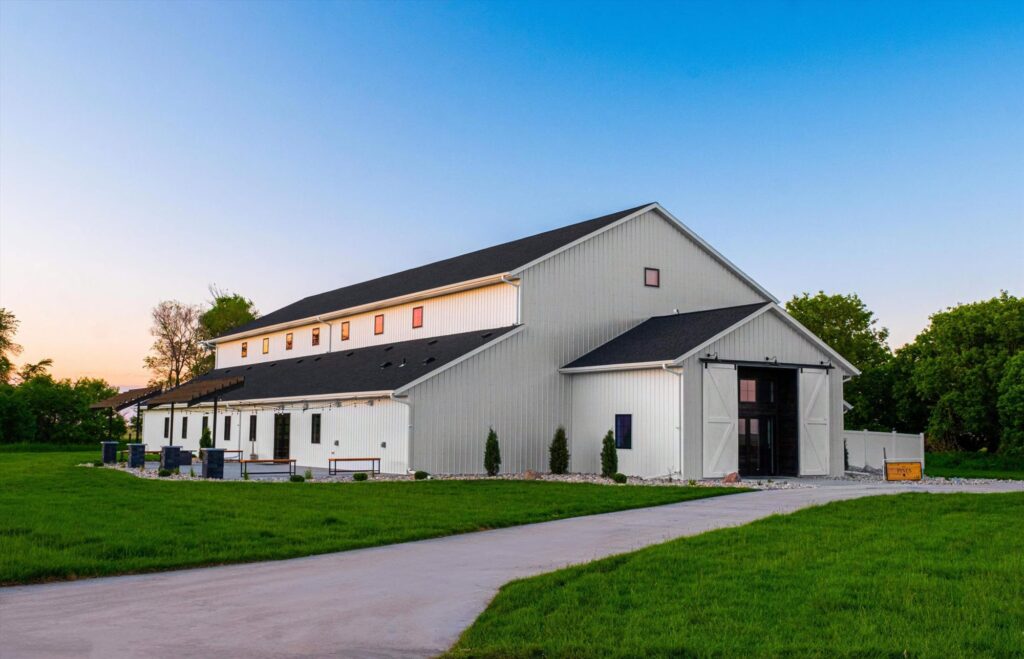 Stunning white barn wedding venue with string lights, perfect for rustic weddings and outdoor celebrations. Angle view with doors open.