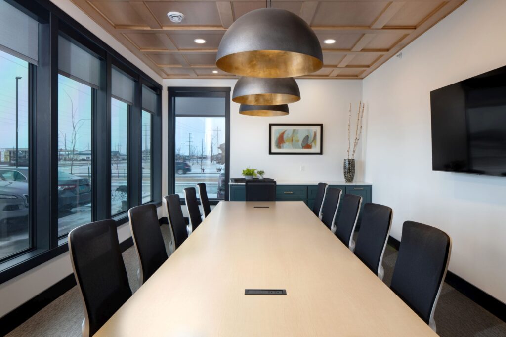Modern corporate boardroom featuring a large conference table, black chairs, stylish lighting, and a wall-mounted TV for presentations.
