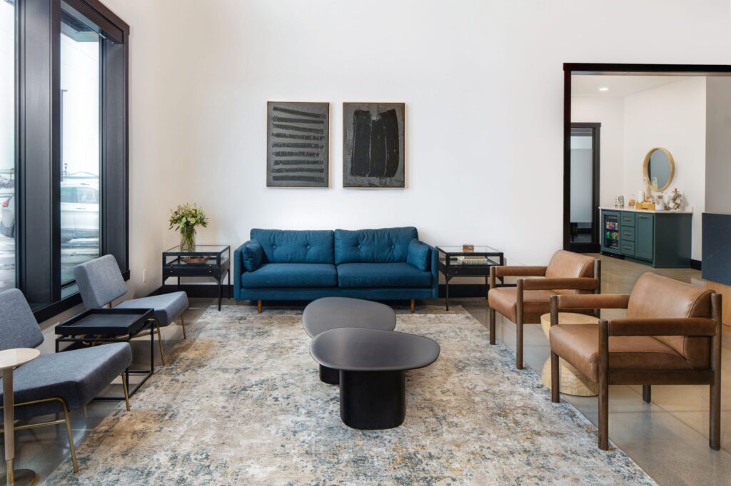 Stylish financial office waiting area with blue sofa, leather chairs, modern art, and patterned rug. Interior design for finance company.