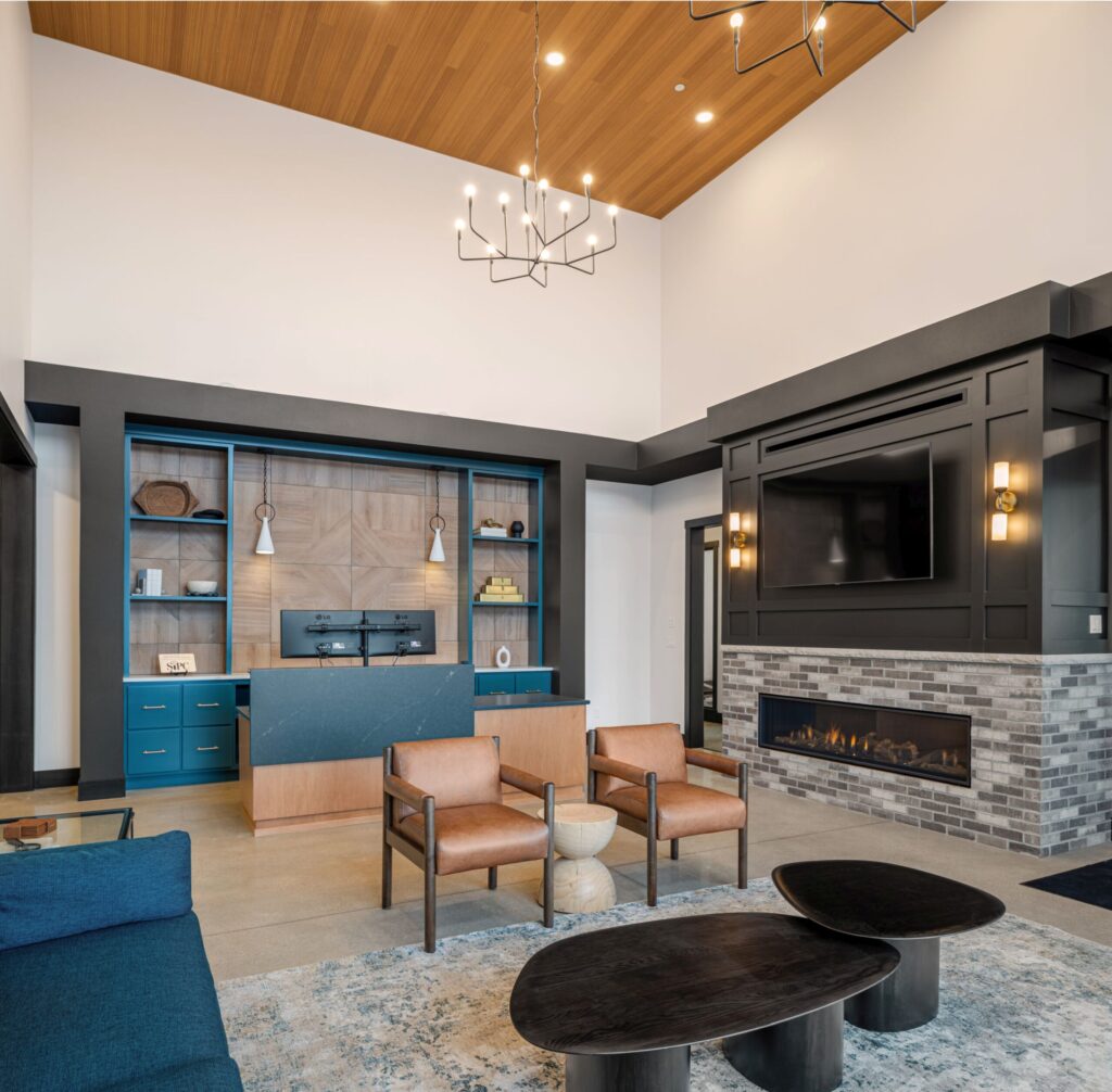 Modern office reception area with sleek desk, dual monitors, custom built-in shelving, a fireplace with a television on the hearth, and stylish pendant lighting.