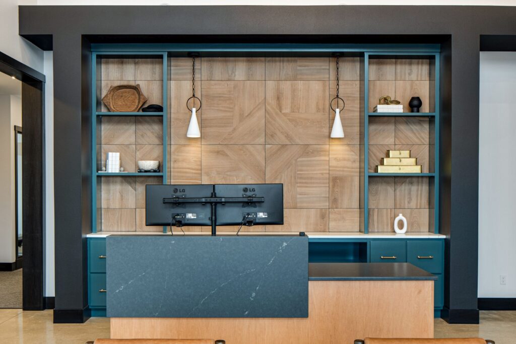 Modern office reception area with sleek desk, dual monitors, custom built-in shelving, and stylish pendant lighting.