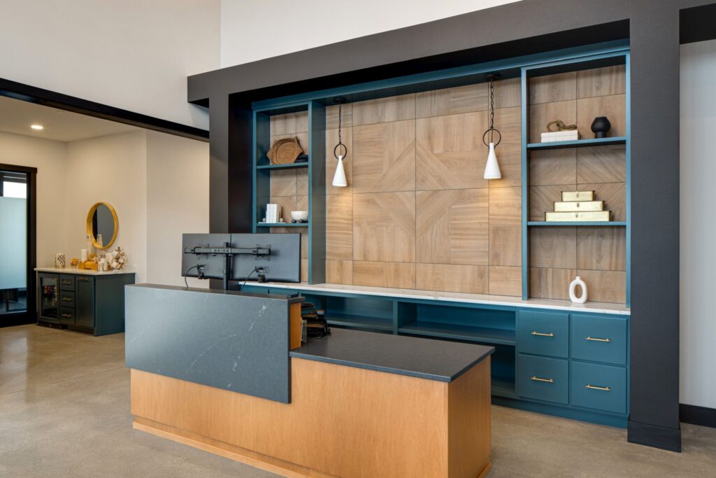 Modern office reception area with sleek desk, dual monitors, custom built-in shelving, and stylish pendant lighting.