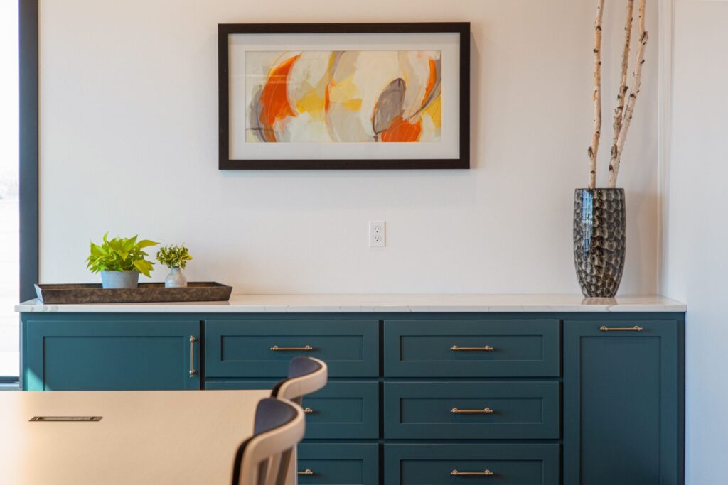 Stylish office interior with teal cabinets, marble countertop, abstract art, and birch branches in a textured vase.