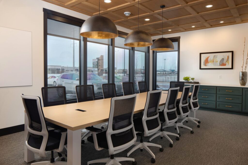 Modern corporate boardroom featuring a large conference table, black chairs, stylish lighting, and large windows.