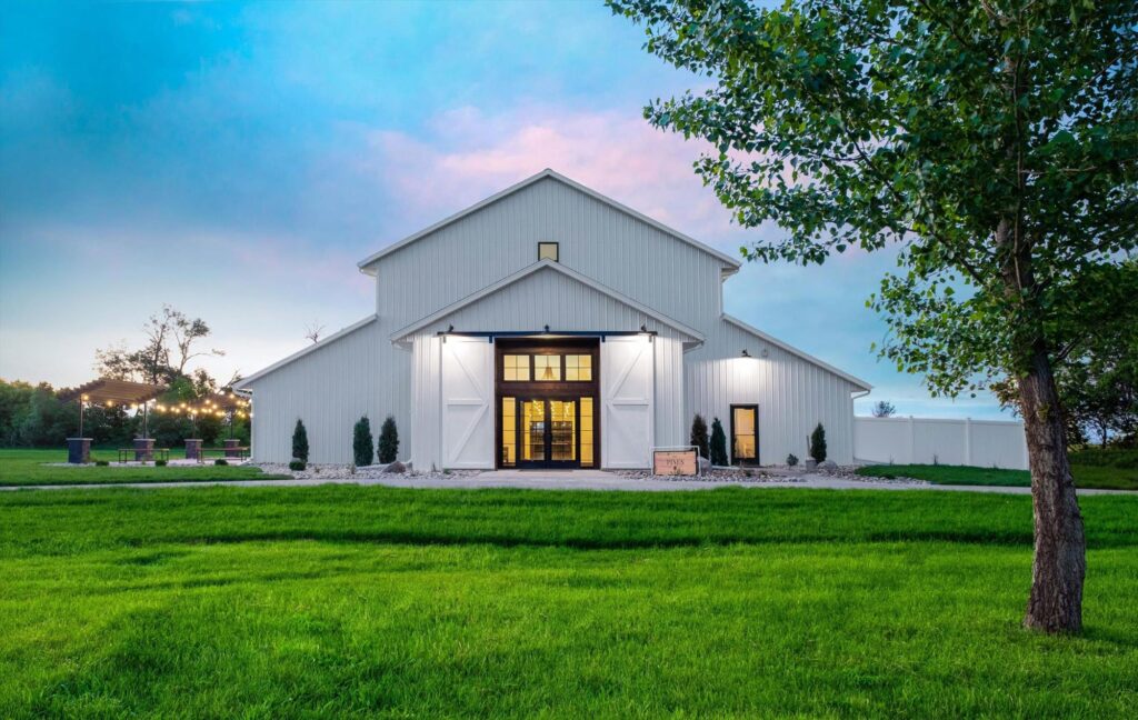 Stunning white barn wedding venue with string lights, perfect for rustic weddings and outdoor celebrations. Front view with doors open.