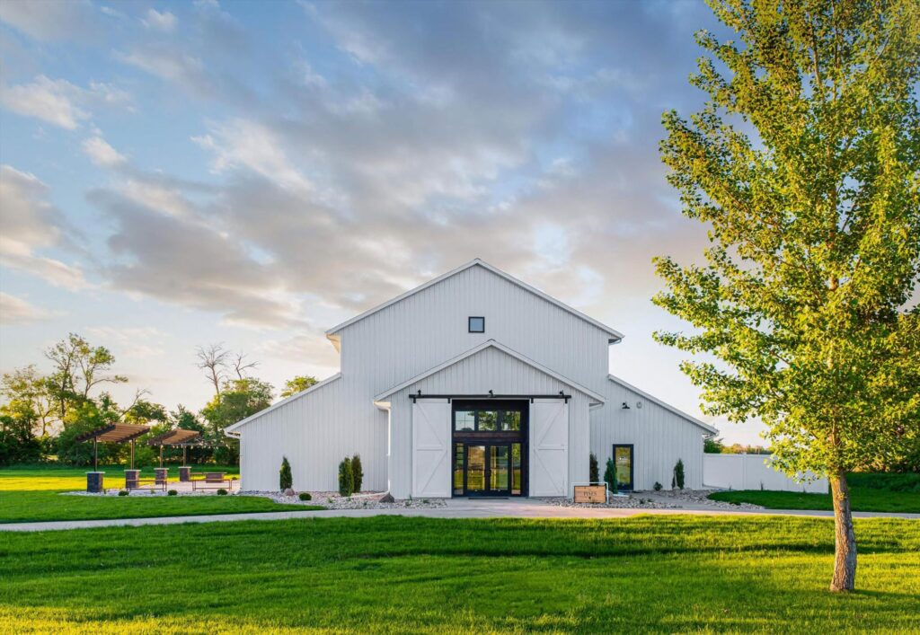 Stunning white barn wedding venue with string lights, perfect for rustic weddings and outdoor celebrations. Front view with doors open.