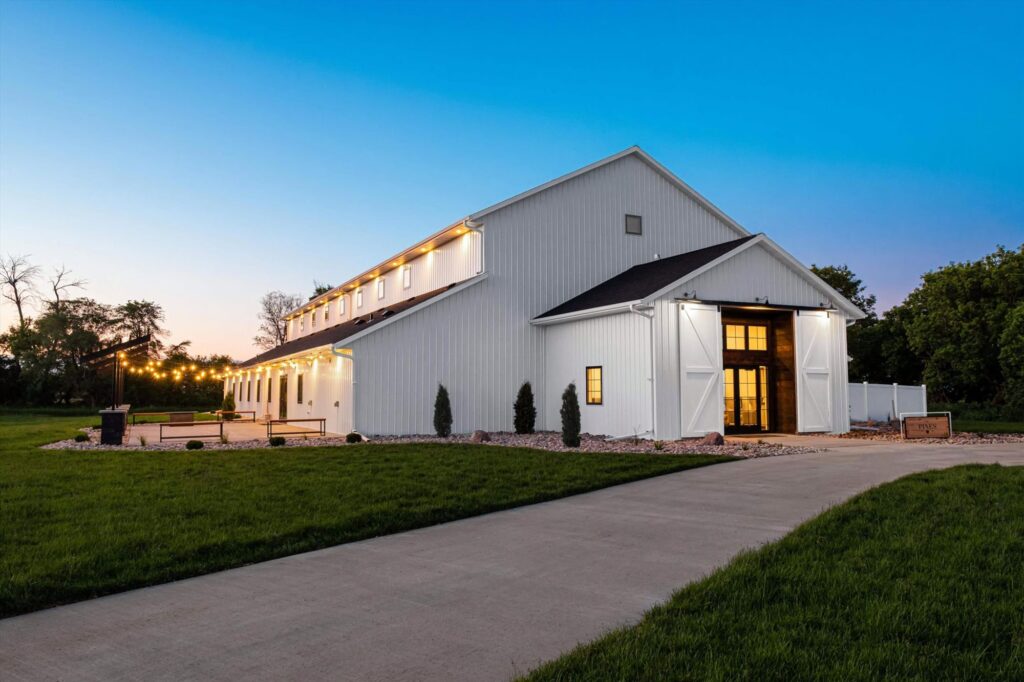 Stunning white barn wedding venue with string lights, perfect for rustic weddings and outdoor celebrations. Twilight sky backdrop.