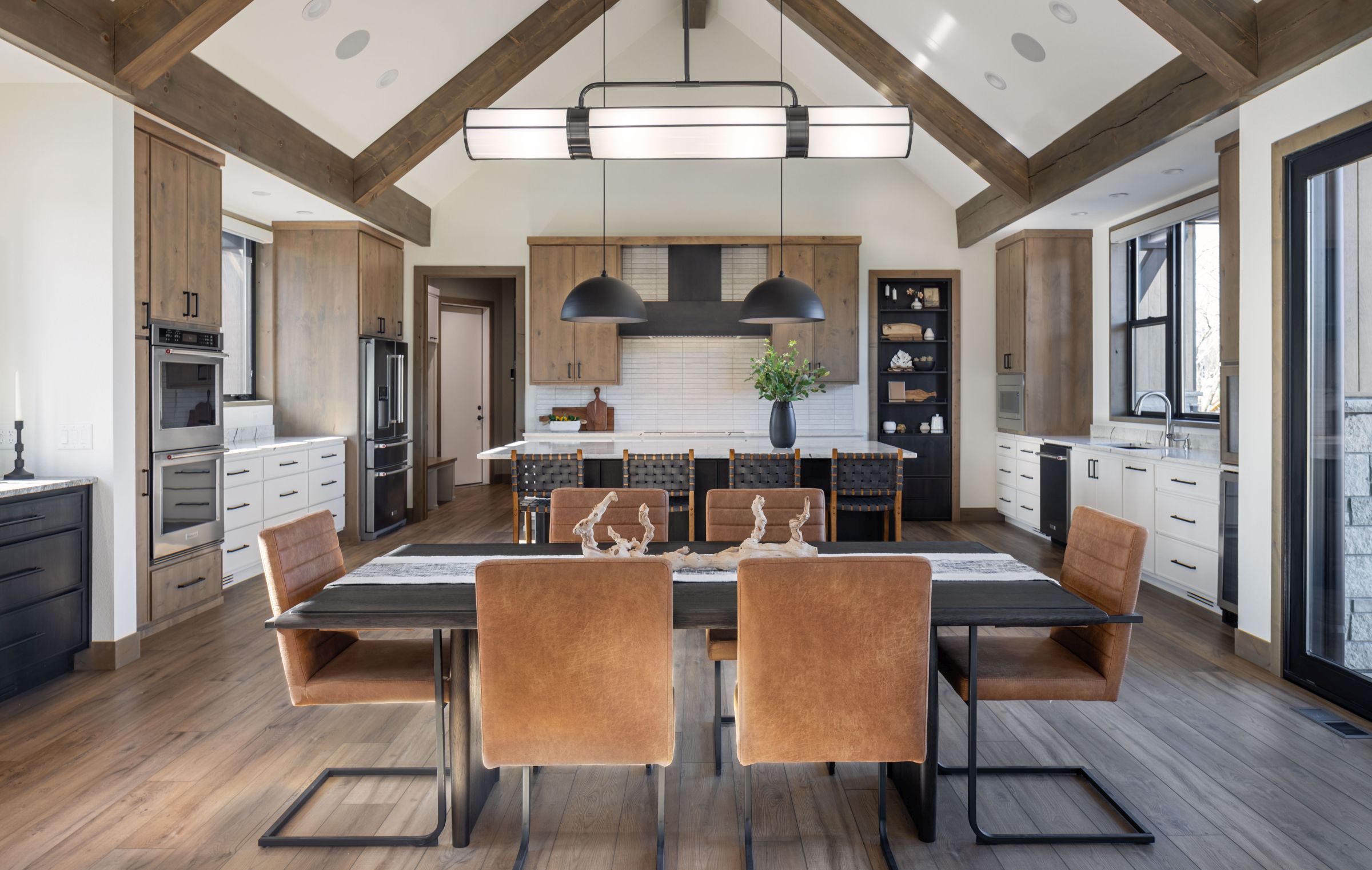 Modern kitchen and dining area with wood floors, cabinets, island, and leather chairs. Bright, open concept home interior.